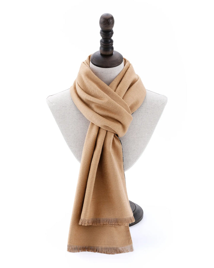 A light tan woven scarf with fringed edges, draped on a light gray fabric mannequin bust with a dark wooden neck cap, set against a plain white background.#color_olive-gold