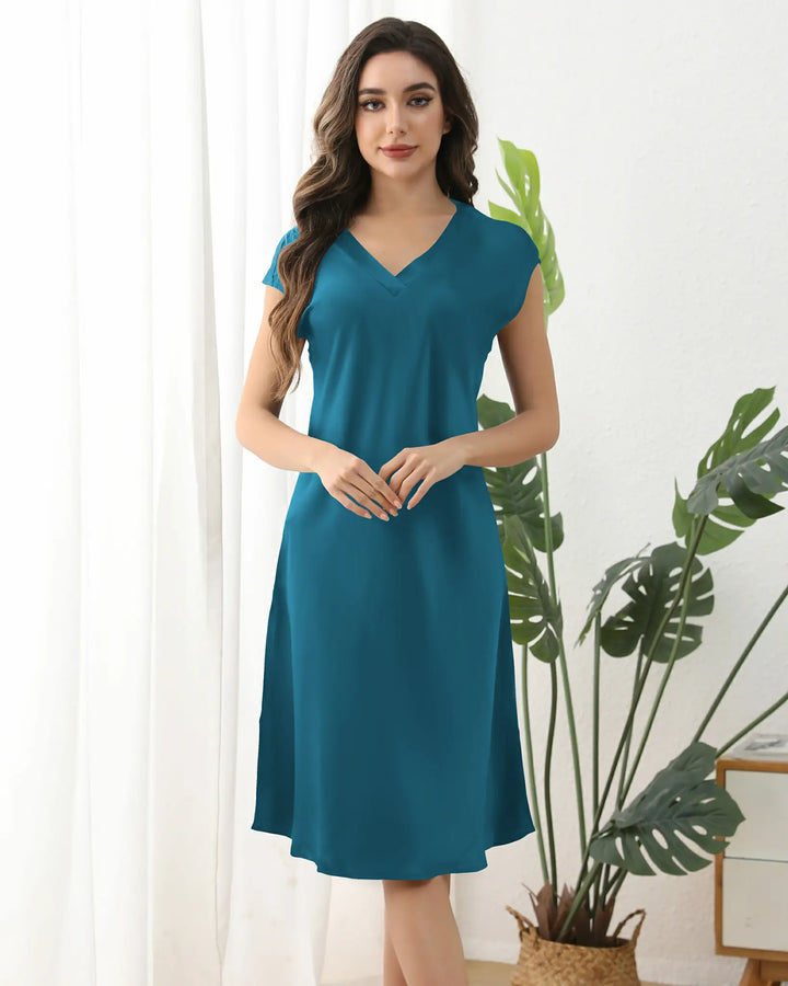 A woman wearing the 22 Momme Comfortable Silk Nightdress by SusanSilk, featuring a teal silk satin fabric and a V-neckline, stands against a plain background, smiling and touching her hair.#color_peacock-blue