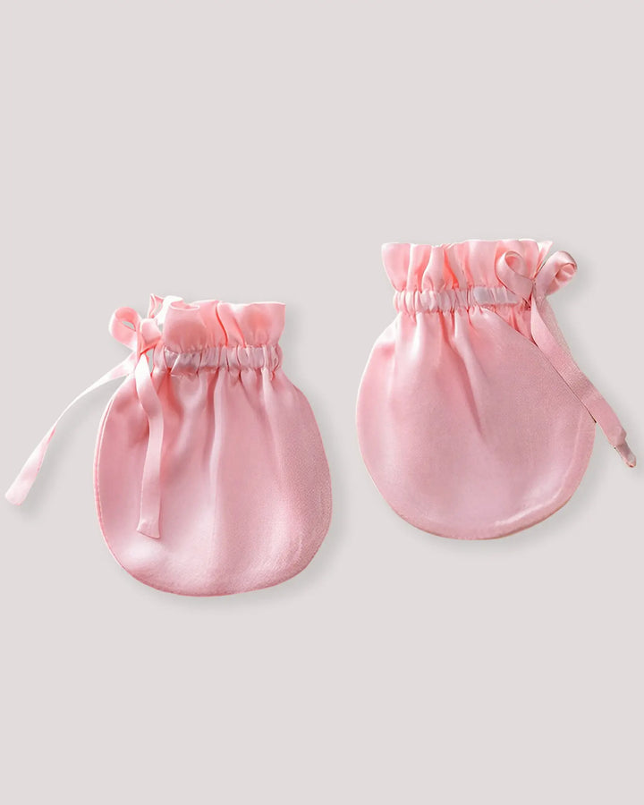 Pair of soft pink mulberry silk baby mittens with an elastic wrist and ribbon closure, designed to reduce scratching while remaining breathable and lightweight.