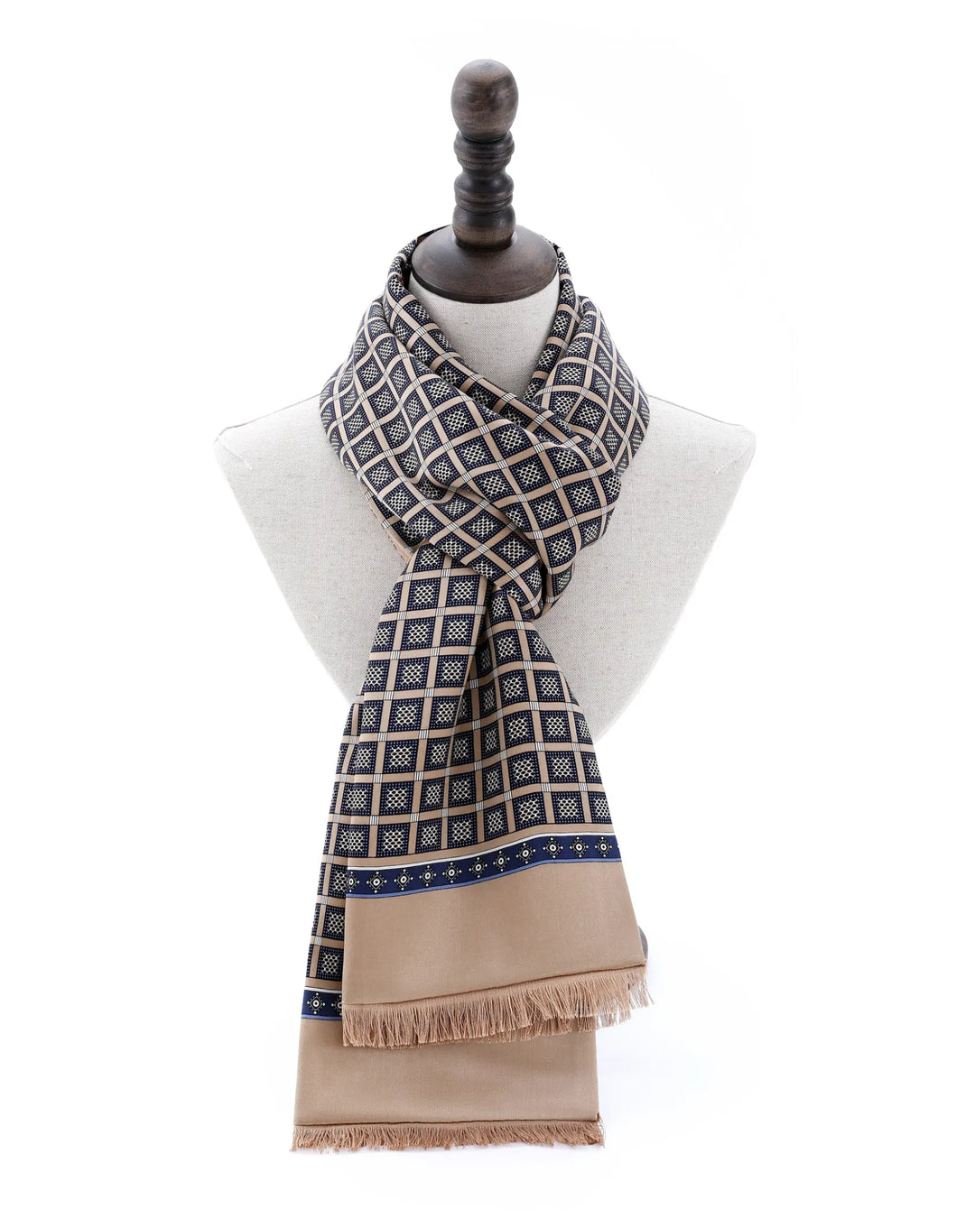 A patterned scarf draped on a cream-colored mannequin torso. The scarf features a geometric grid pattern in navy blue and beige, with a solid beige lower section and fringe.#color_antique-gold