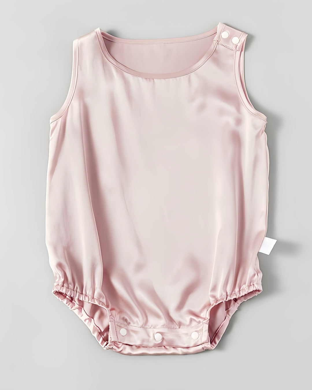 The 19 Momme Silk Baby Button Onesie by SusanSilk is a pale pink baby romper made from soft silk, featuring snap closures at the shoulder and bottom.