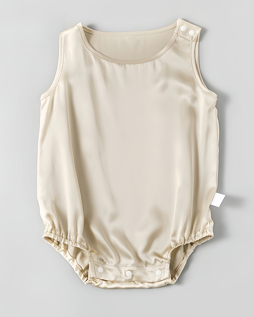 The 19 Momme Silk Baby Button Onesie by SusanSilk is a sleeveless, light beige baby romper made from soft silk, featuring a round neckline, shoulder snap buttons, and bottom snap closures.