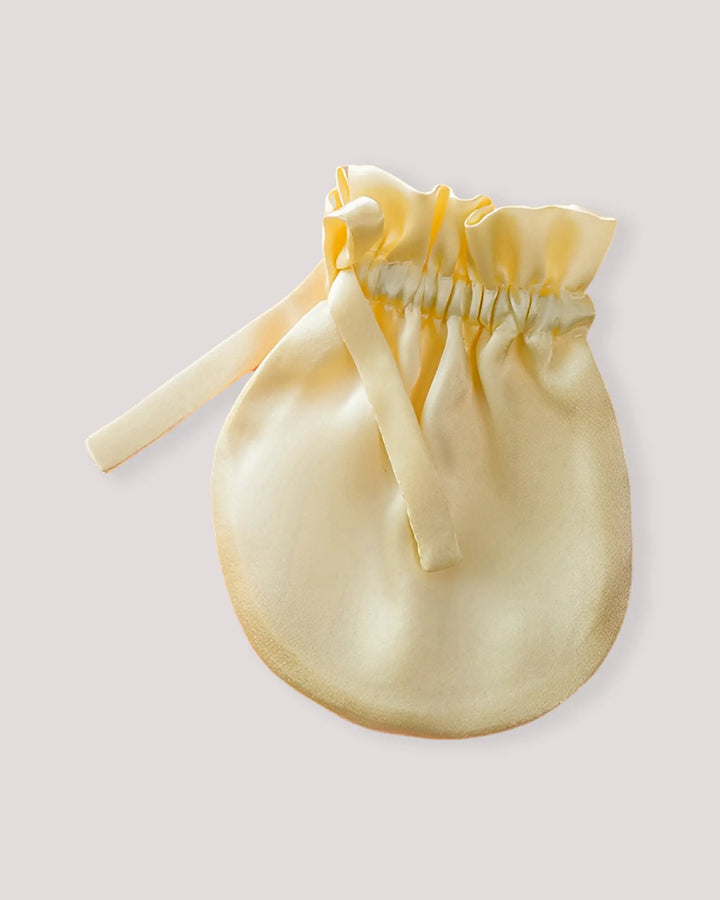 Close-up of yellow 19 Momme mulberry silk baby mittens with an elastic cuff and ribbon tie, designed for newborn comfort and anti-scratch protection.
