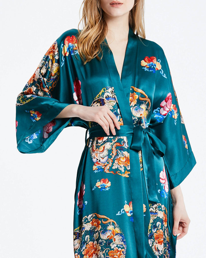 A person wearing the Wheel of Fortune Long Silk Kimono by SusanSilk, showcasing a vibrant teal satin fabric adorned with colorful floral and dragon patterns, complete with wide sleeves and a waist belt.#color_sea-green