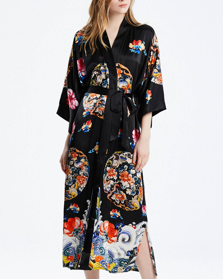 A person wearing the SusanSilk "Wheel of Fortune" long black silk kimono, adorned with colorful floral and circular patterns, stands against a plain white background.#color_black