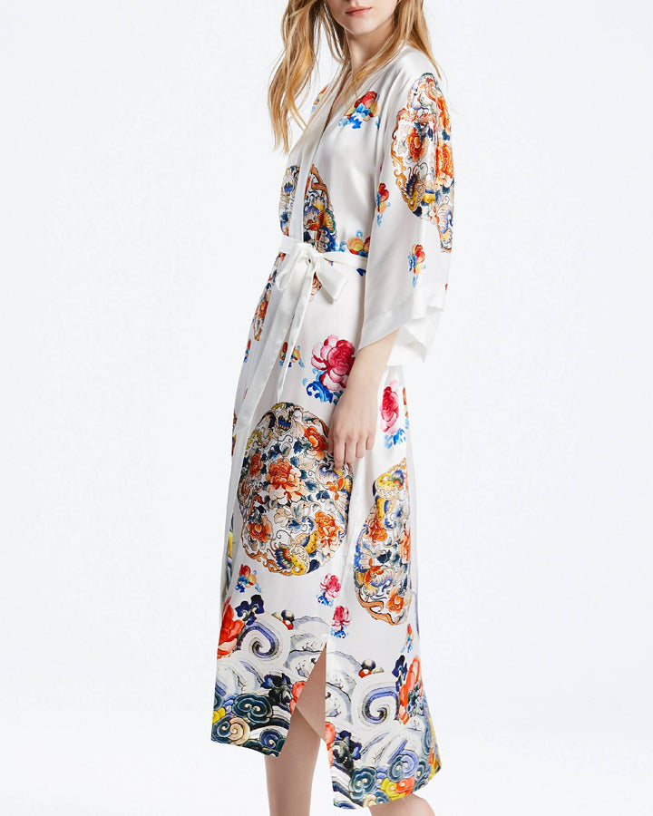 Person standing sideways wearing the Wheel of Fortune Long Silk Kimono by SusanSilk, adorned with colorful, intricate floral and abstract designs. The kimono features a tied belt and a side slit.#color_white