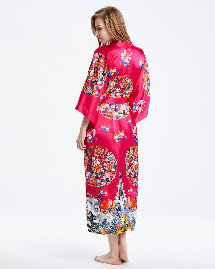 A person wearing a luxurious red Wheel of Fortune Long Silk Kimono by SusanSilk, adorned with colorful, intricate designs, stands barefoot, facing away from the camera.#color_rose-red