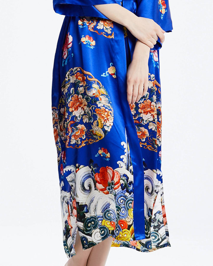 A person wearing the Wheel of Fortune Long Silk Kimono, a blue floral patterned masterpiece from SusanSilk, with hands crossed gently in front, epitomizes the elegance found in their exclusive collection.#color_royal-blue