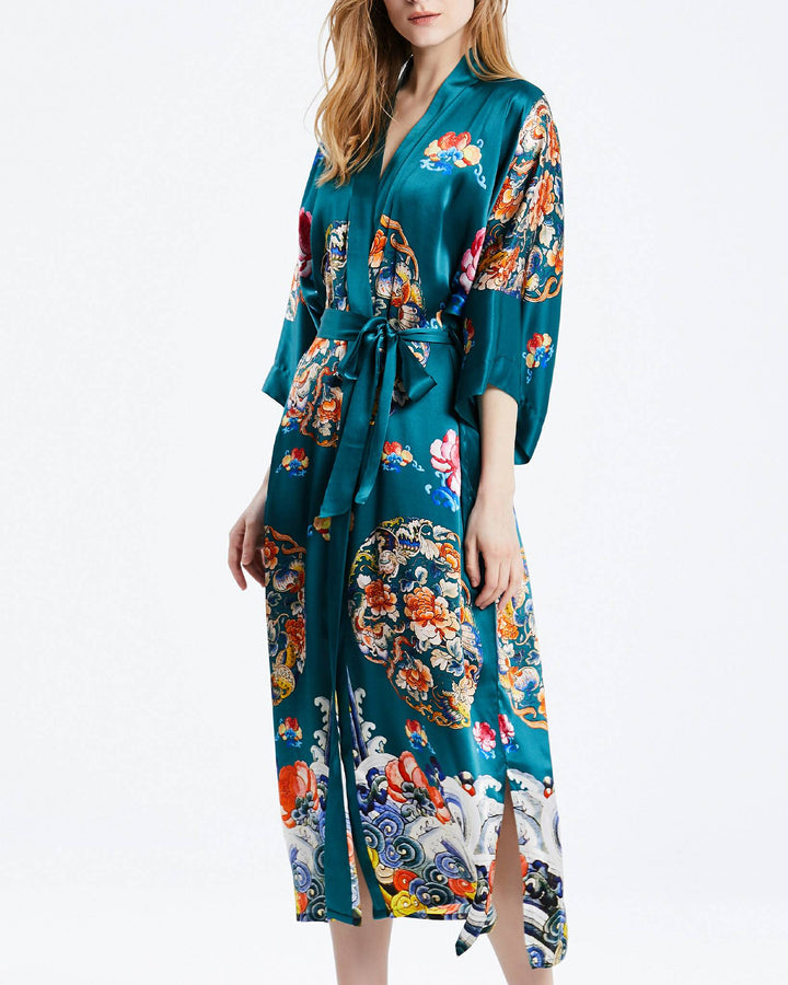 A person wearing the Wheel of Fortune Long Silk Kimono from SusanSilk, a luxurious teal robe adorned with colorful floral and artistic patterns, featuring a waist tie and side slits.#color_sea-green