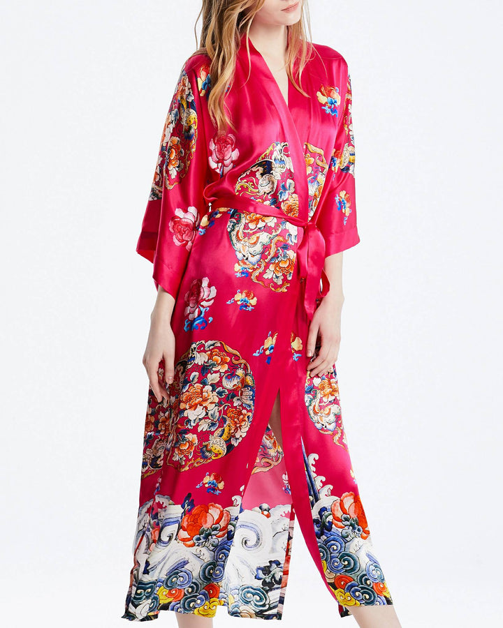 A person wearing the vibrant Wheel of Fortune Long Silk Kimono by SusanSilk, adorned with a floral pattern in red, stands against a plain white background.#color_rose-red