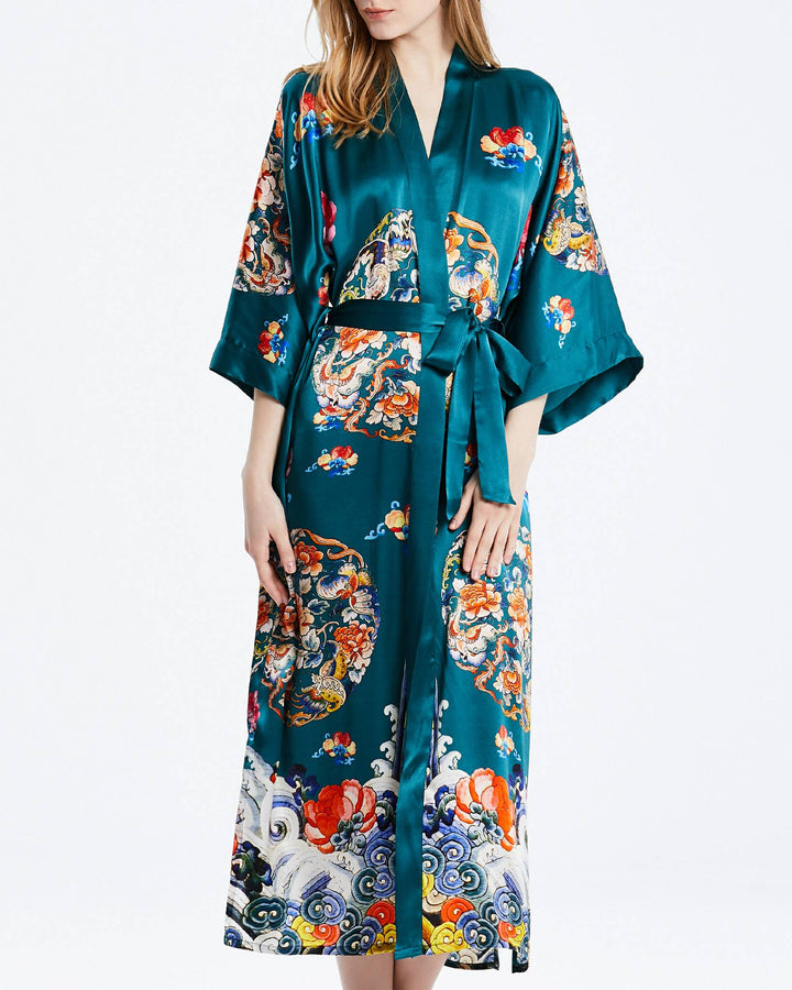 A person wearing the Wheel of Fortune Long Silk Kimono by SusanSilk, featuring colorful and intricate patterns with a sash belt, stands against a plain white background.#color_sea-green