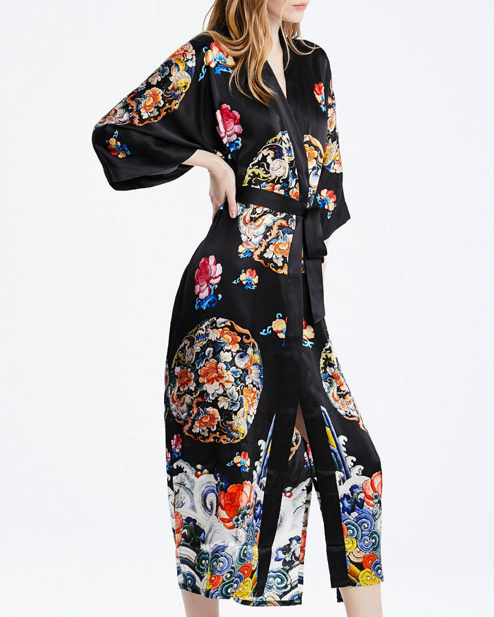 A person wearing the Wheel of Fortune Long Silk Kimono by SusanSilk, adorned with colorful patterns, stands against a plain white background, reminiscent of the brand's elegance.#color_black