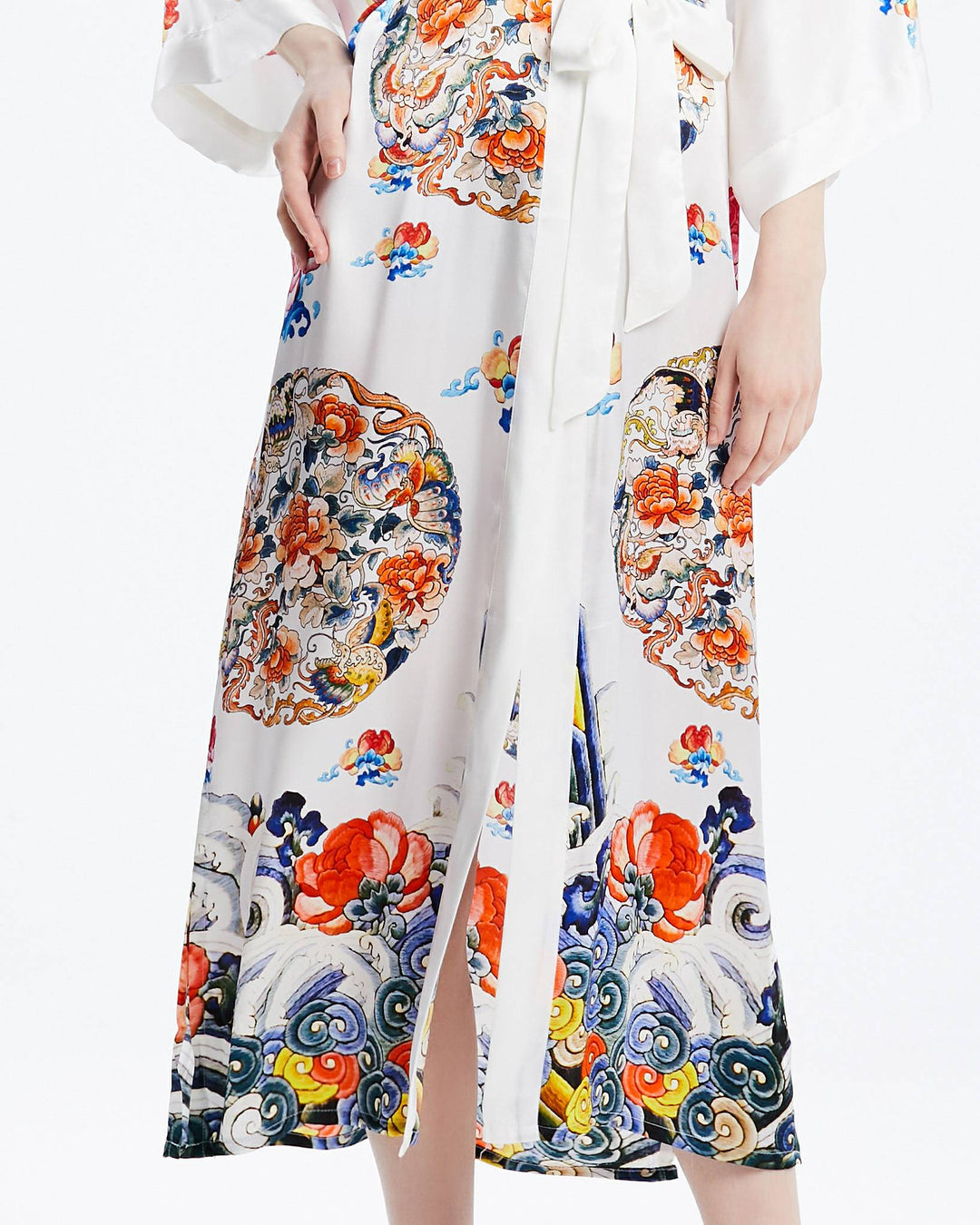 A person wearing the Wheel of Fortune Long Silk Kimono from SusanSilk, adorned with colorful floral patterns, featuring a front slit and a tied waist sash. The luxurious susansilk fabric drapes elegantly, highlighting the lower half of their body.#color_white