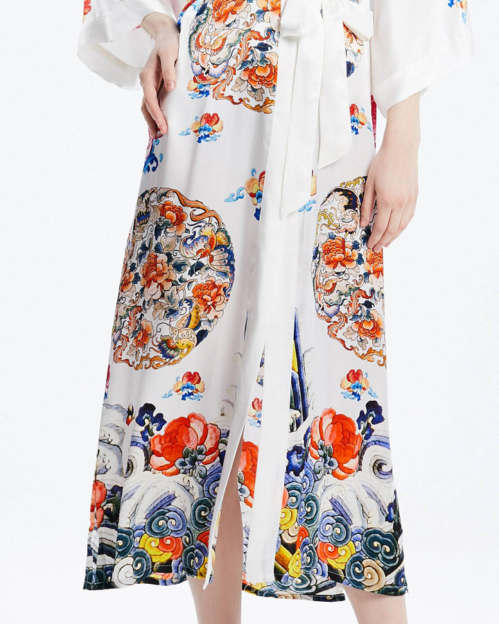 A person wearing the Wheel of Fortune Long Silk Kimono from SusanSilk, adorned with colorful floral patterns, featuring a front slit and a tied waist sash. The luxurious susansilk fabric drapes elegantly, highlighting the lower half of their body.#color_white