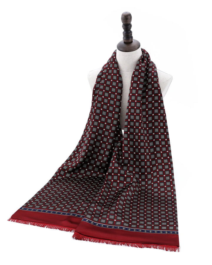 A long patterned scarf draped on a white dress form mannequin against a plain white background. The scarf features a small geometric checkered pattern in red, gray, and black, with a solid red border and fringed ends.#color_wine-red