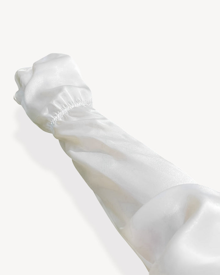 A person’s arm, wearing SusanSilk's Sun Protection Silk Over Sleeves with an elastic cuff, stretched outward against a light gray background, highlights the delicate texture of the material.