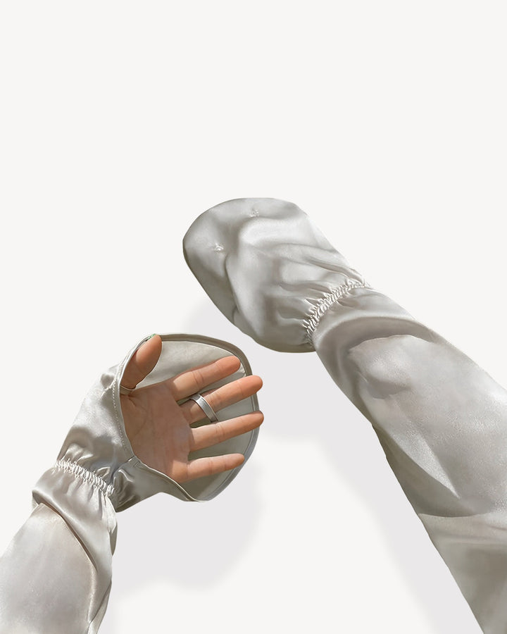 A close-up image showcases a hand adorned with SusanSilk's sheer, white, Sun Protection Silk Over Sleeves, featuring openings at the palm and fingers, set against a light background.