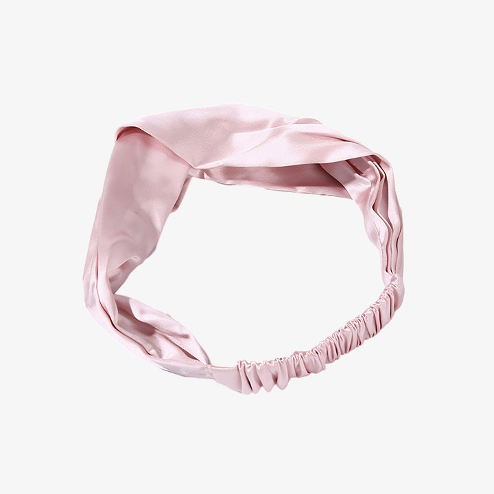 A Pure Color Criss Cross Silk Headband by SusanSilk, featuring a pink satin material with a twisted knot design at the front and elastic at the back.