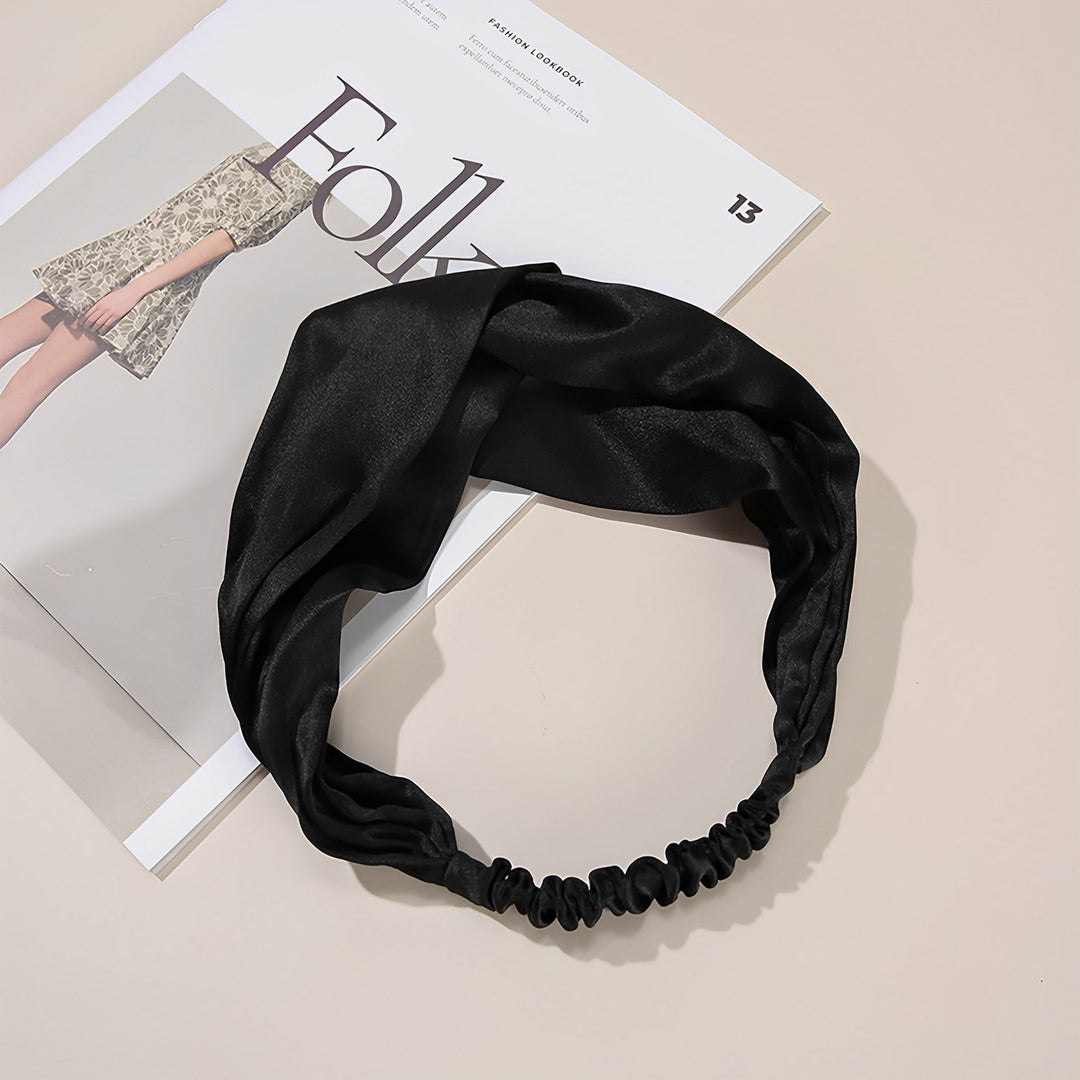 A Pure Color Criss Cross Silk Headband from SusanSilk is laid out on top of an open fashion magazine on a beige surface.