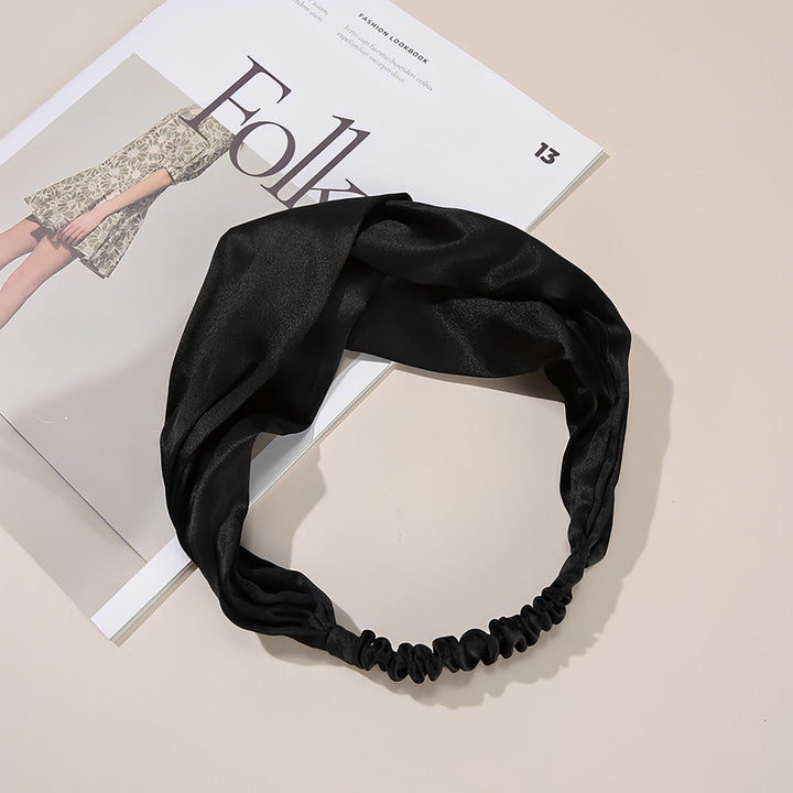 A Pure Color Criss Cross Silk Headband from SusanSilk is laid out on top of an open fashion magazine on a beige surface.