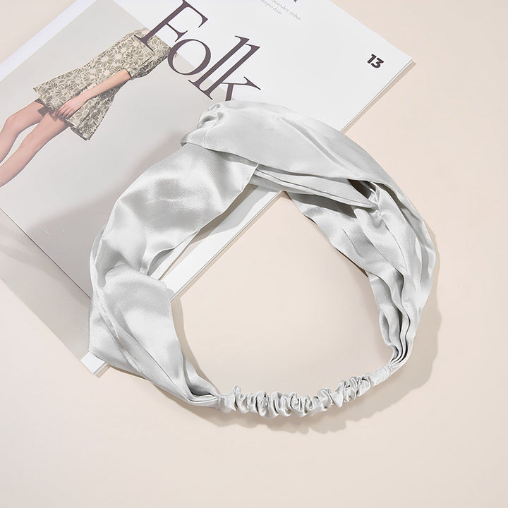 A white, Pure Color Criss Cross Silk Headband from SusanSilk graces the pages of an open magazine, highlighting a fashion article featuring a model in a beige dress.