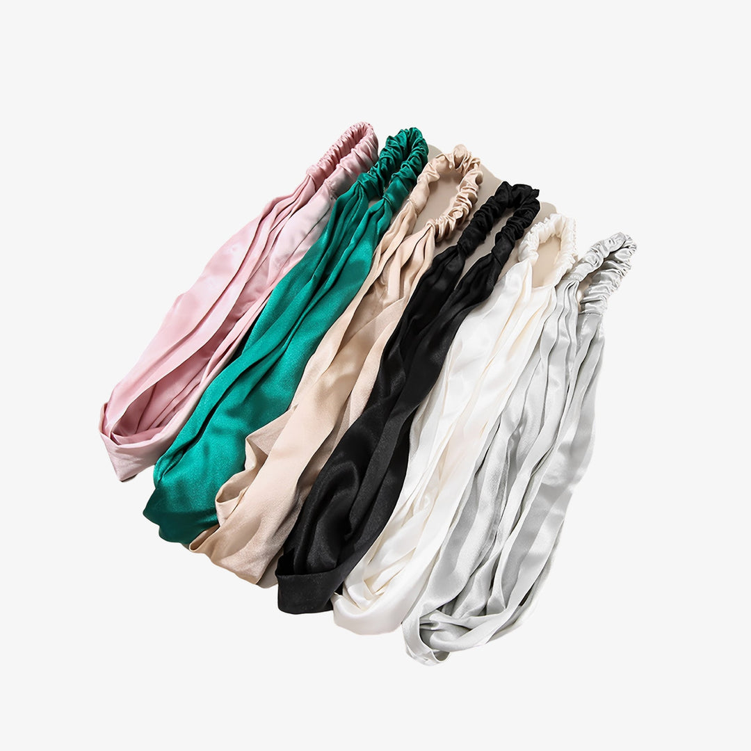 Seven luxurious Pure Color Criss Cross silk headbands by SusanSilk, available in an array of colors including pink, green, beige, black, white, and gray, are beautifully displayed in a row.