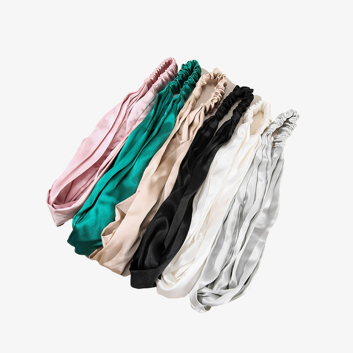Seven luxurious Pure Color Criss Cross silk headbands by SusanSilk, available in an array of colors including pink, green, beige, black, white, and gray, are beautifully displayed in a row.