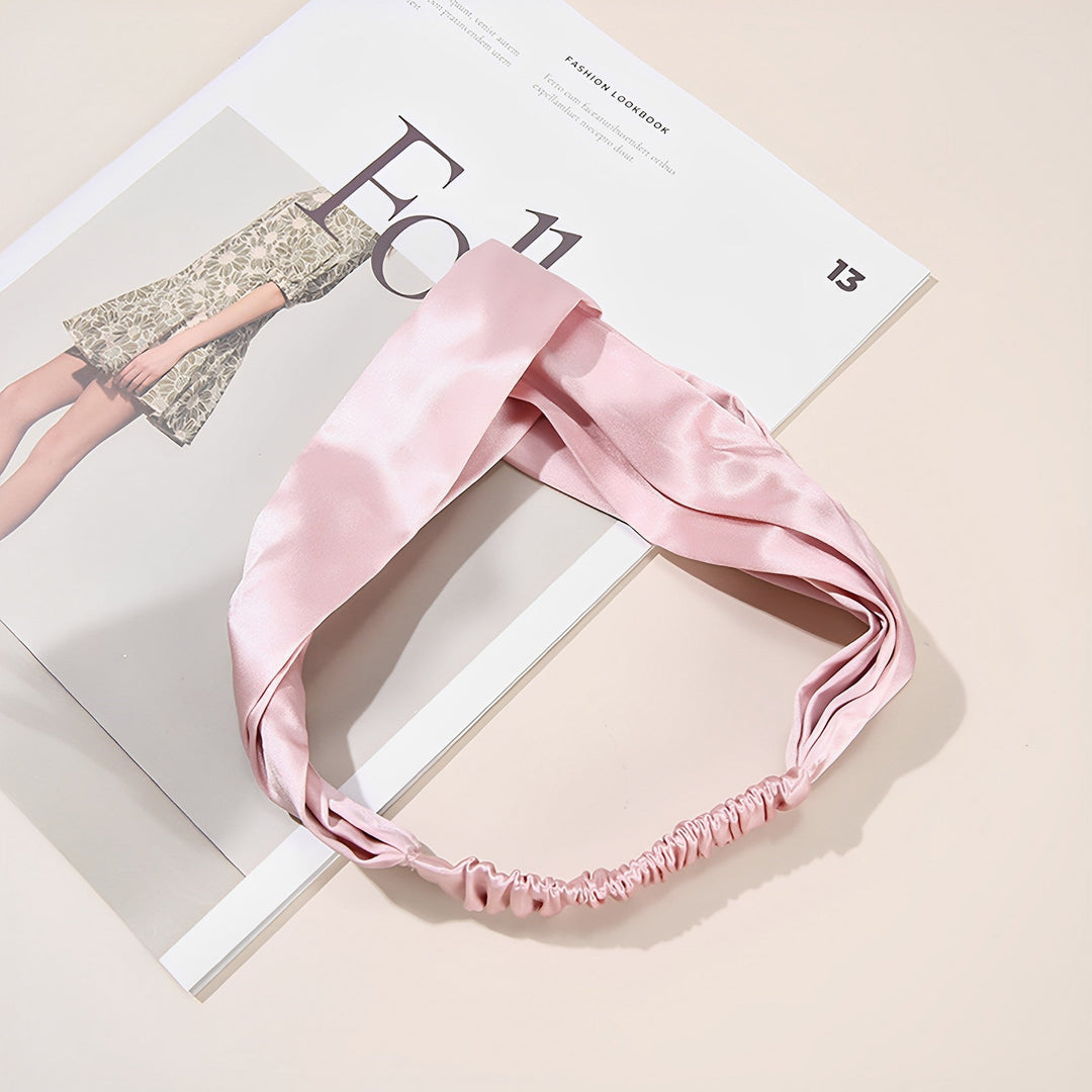 A Pure Color Criss Cross Silk Headband from SusanSilk lies on top of an open magazine featuring a fashion model draped in luxurious silk.