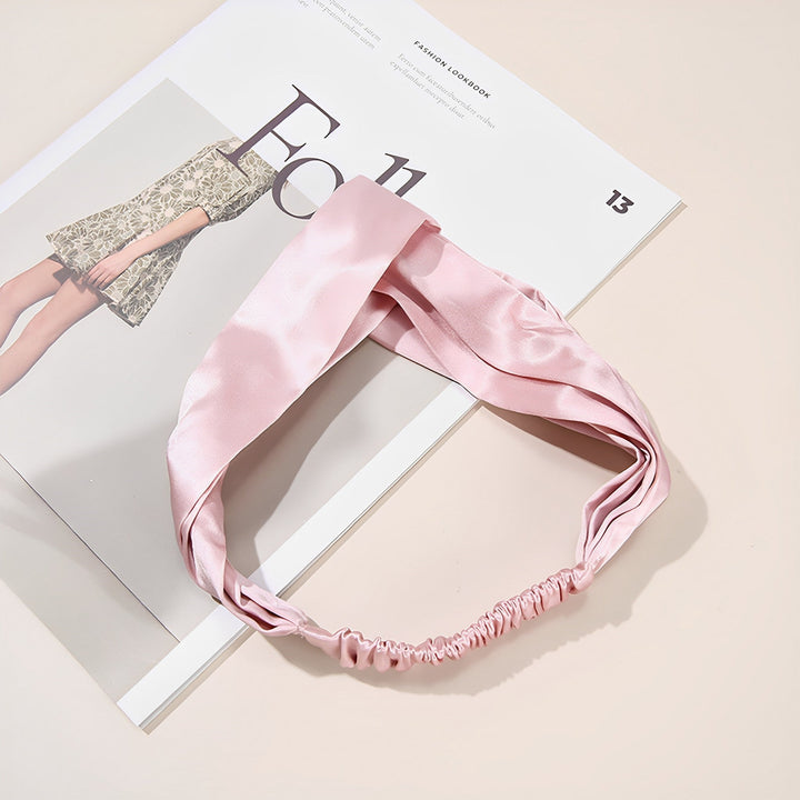 A Pure Color Criss Cross Silk Headband from SusanSilk lies on top of an open magazine featuring a fashion model draped in luxurious silk.