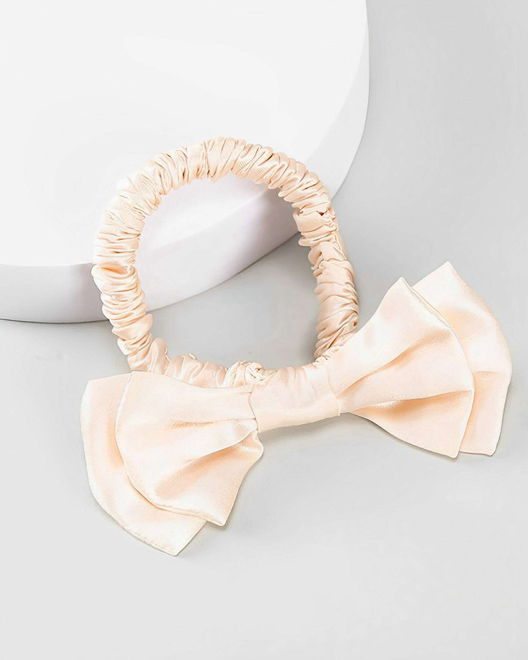 A cream-colored Vintage Bow-Knot Silk Scrunchie, elegantly crafted by SusanSilk, is placed on a light gray surface.