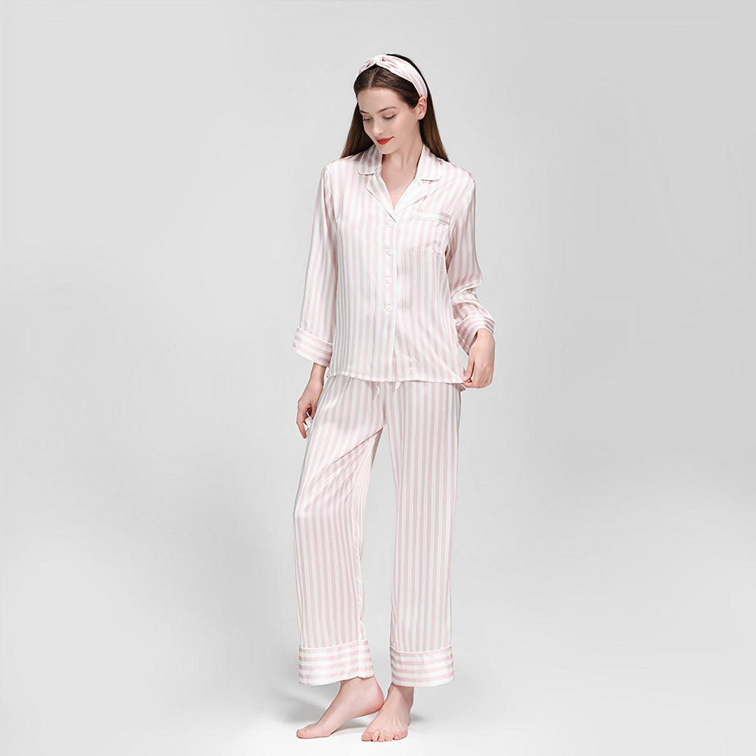 A woman wearing SusanSilk's 19 Momme Chic Stripe Silk Pajamas Set and a matching headband stands barefoot against a plain white background.