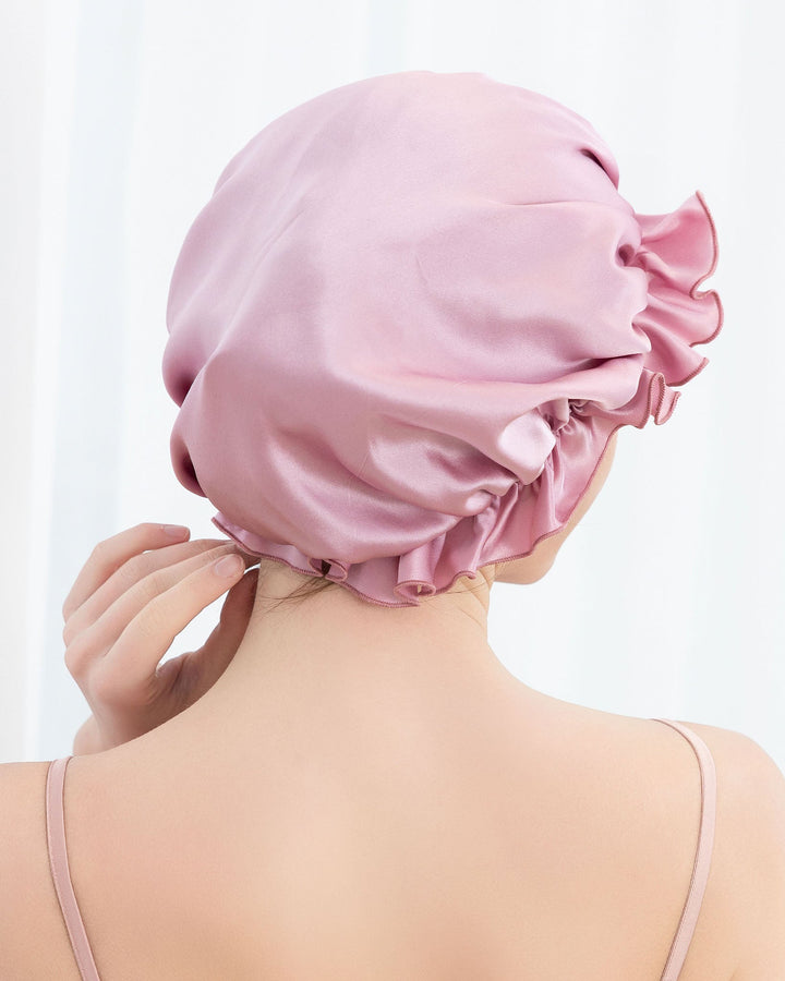 A person wearing a Flounced Silk Bonnet For Sleeping by SusanSilk, seen from the back with one hand gently touching the silky cap.