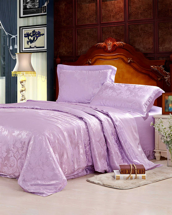 A bedroom with an ornate wooden headboard, a 19 Momme Jacquard Silk Bedding Set - 4Pcs by SusanSilk in lavender, a beige rug with a stack of books, a flower vase from SusanSilk, and a lamp on the left side.