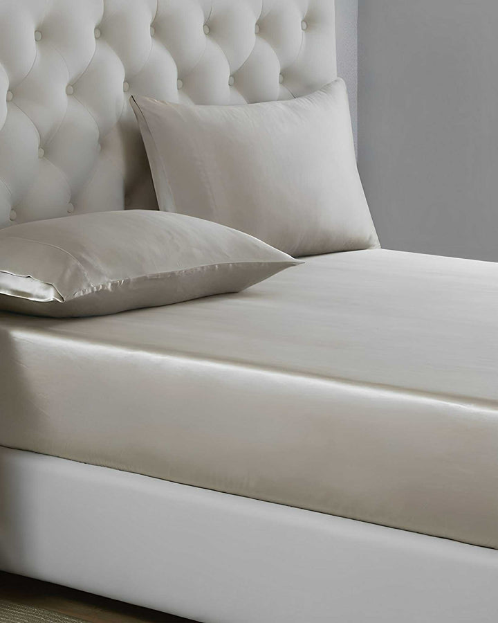 A neatly made bed with a tufted headboard, featuring the 19 Momme Moisturizing Silk Bedding Set - 4Pcs by SusanSilk in beige satin and two matching pillows.