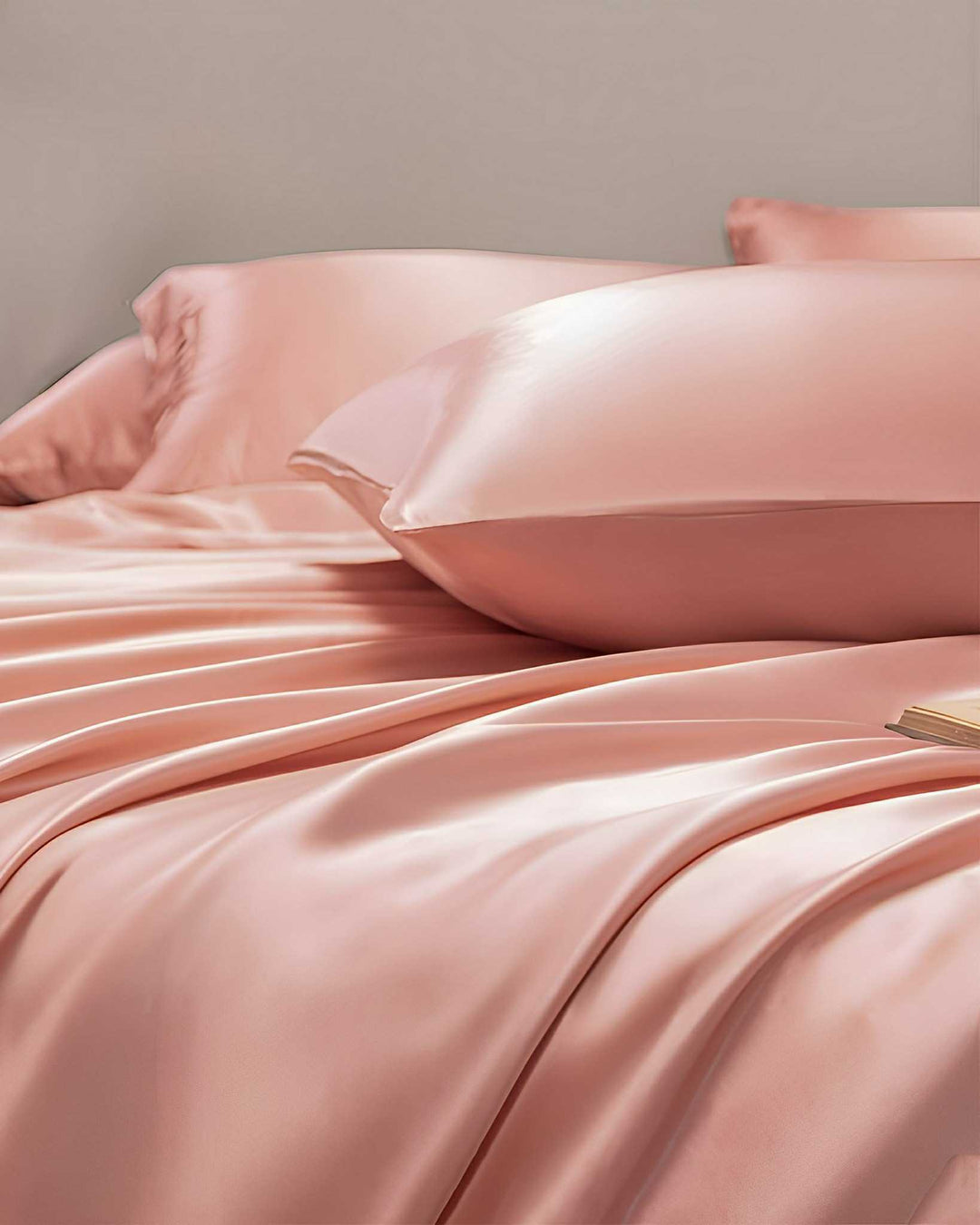 A close-up of a bed featuring the SusanSilk 19 Momme Moisturizing Silk Bedding Set - 4Pcs, with smooth, light pink satin sheets and pillowcases, exuding an undeniable sense of luxury.