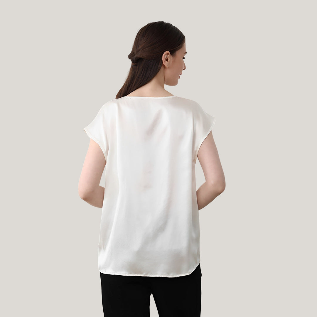 A woman with long brown hair is facing away, showcasing a loose-fitting Short Sleeves Round Neck Silk Tee by SusanSilk in white, paired with black pants against a plain background.