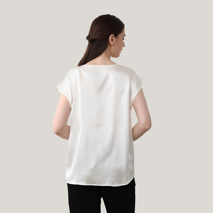 A woman with long brown hair is facing away, showcasing a loose-fitting Short Sleeves Round Neck Silk Tee by SusanSilk in white, paired with black pants against a plain background.