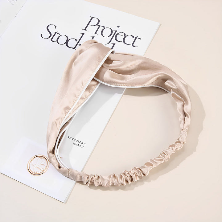 A beige satin headband, the Piping Criss Cross Silk Headband by SusanSilk, lies on a magazine opened to an article titled "Project Stocked." A round gold accessory is placed near the bottom left corner, effortlessly complementing the SusanSilk headband.