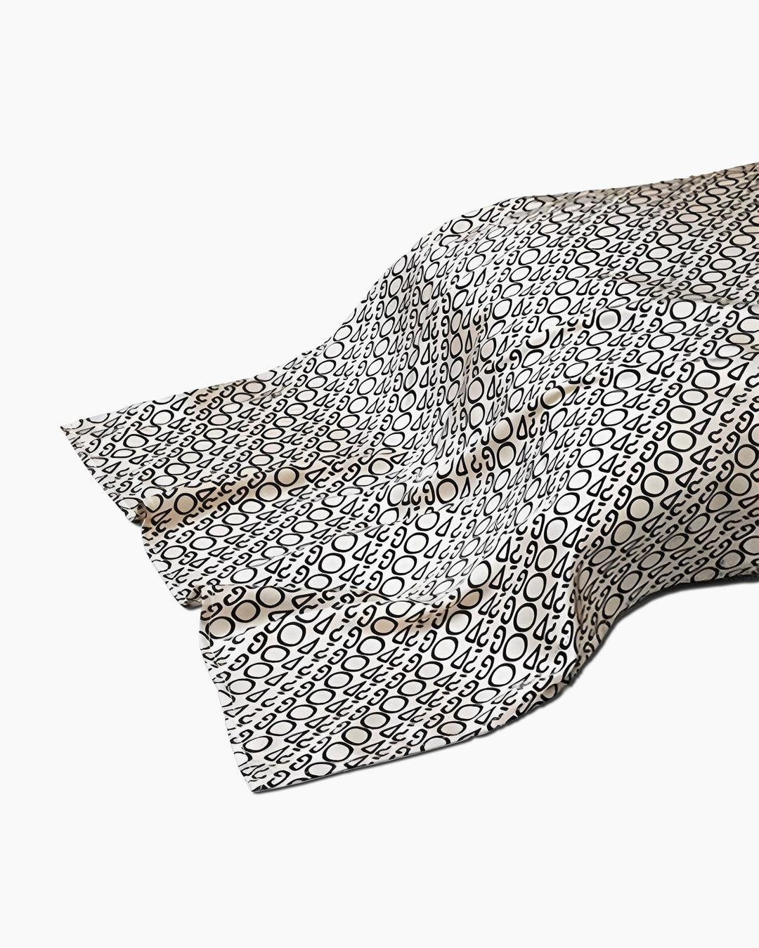 A piece of SusanSilk's 19 Momme Printing Silk Pillow Cover, draped and wrinkled, featuring a pattern of black and white circles and ovals.