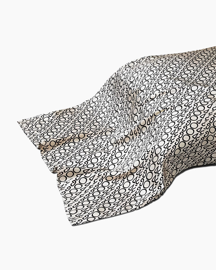 A piece of SusanSilk's 19 Momme Printing Silk Pillow Cover, draped and wrinkled, featuring a pattern of black and white circles and ovals.