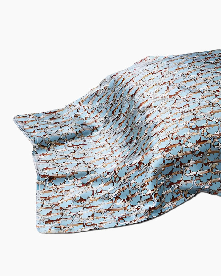 A 19 Momme Printing Silk Pillow Cover by SusanSilk, featuring a light blue hue with an intricate pattern of brown and beige intertwining shapes, draped gracefully against a white background.