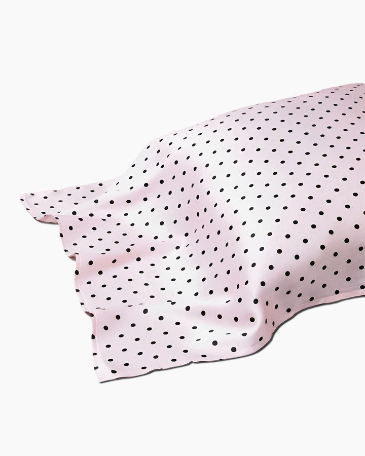 A 19 Momme Printing Silk Pillow Cover in pink, featuring black polka dots and partially laid out with visible wrinkles, evocative of the luxurious textures from SusanSilk.