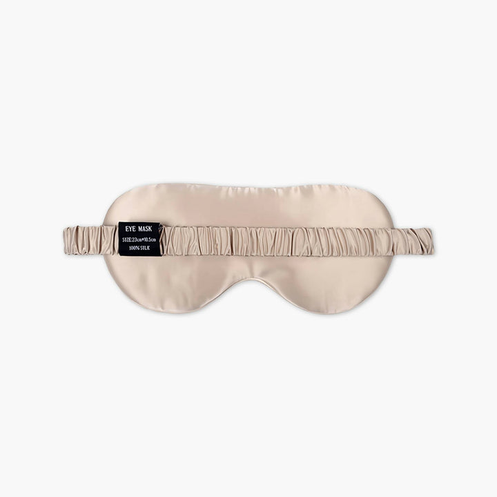 An elegant silk eye mask called "Golden Pyramid" in beige, featuring a ruched elastic strap. A black tag on the strap reads "EYE MASK - SLEEP WITH US by SusanSilk.