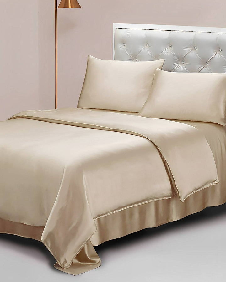 A neatly made bed with 19 Momme Seamless Silk Duvet Cover by SusanSilk, cream-colored sheets, silk pillows, and a tufted headboard. A copper-colored floor lamp stands beside the bed.