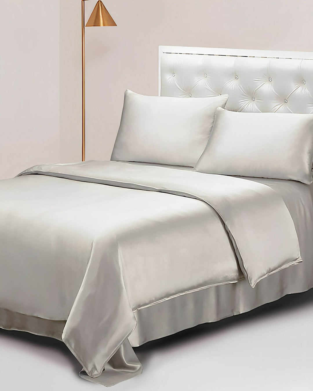 A bed featuring the luxurious SusanSilk 19 Momme Seamless Silk Duvet Cover in gray, accompanied by a comforter, two pillows, and a tufted headboard, is positioned next to a floor lamp with a gold stand and a conical shade.