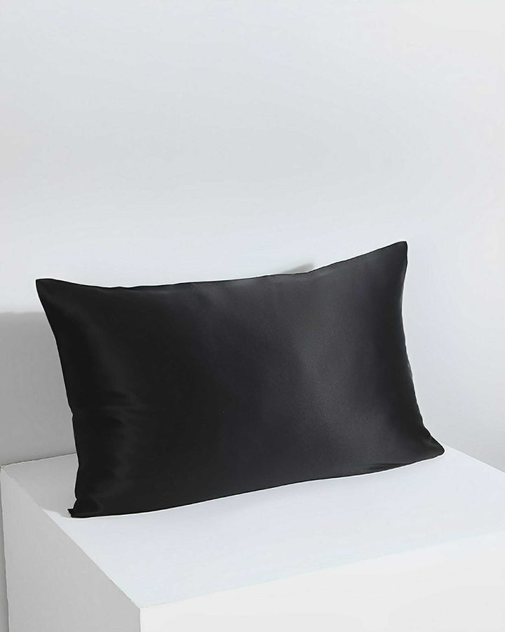The 19 Momme Silk Pillowcase Zipper by SusanSilk in black, featuring a smooth silk surface, is placed on a white surface against a white background.