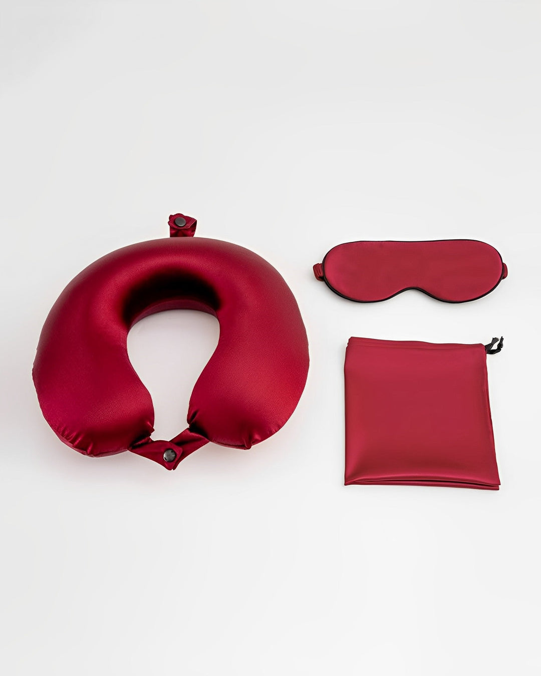 The 19 Momme Silk U-Shaped Pillow Travel Set by SusanSilk, crafted from luxurious red silk, includes a neck pillow, an eye mask, and a rectangular pouch, all arranged neatly against a white background.
