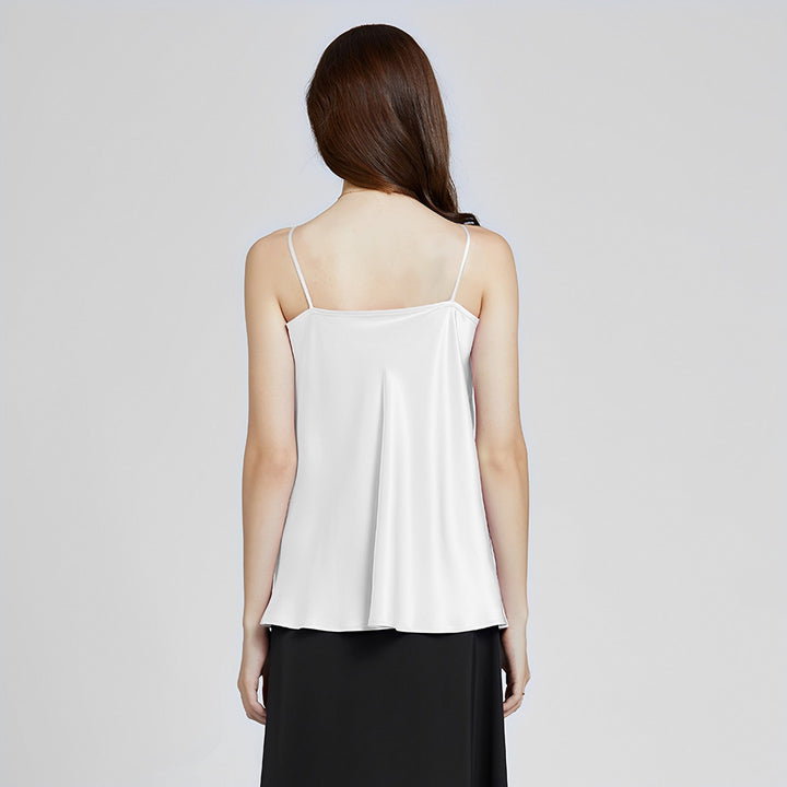 A woman with long brown hair is standing with her back to the camera, wearing a white Elegant Cowl Neck Silk Camisole by SusanSilk and a black skirt.