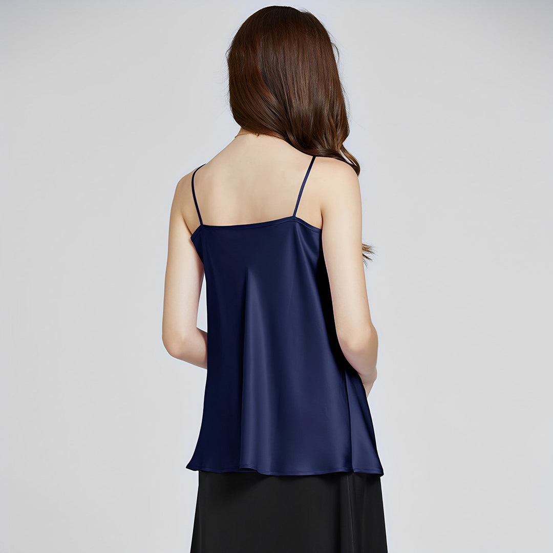 A woman with long brown hair is facing away from the camera, wearing an Elegant Cowl Neck Silk Camisole in navy blue by SusanSilk and a black skirt.