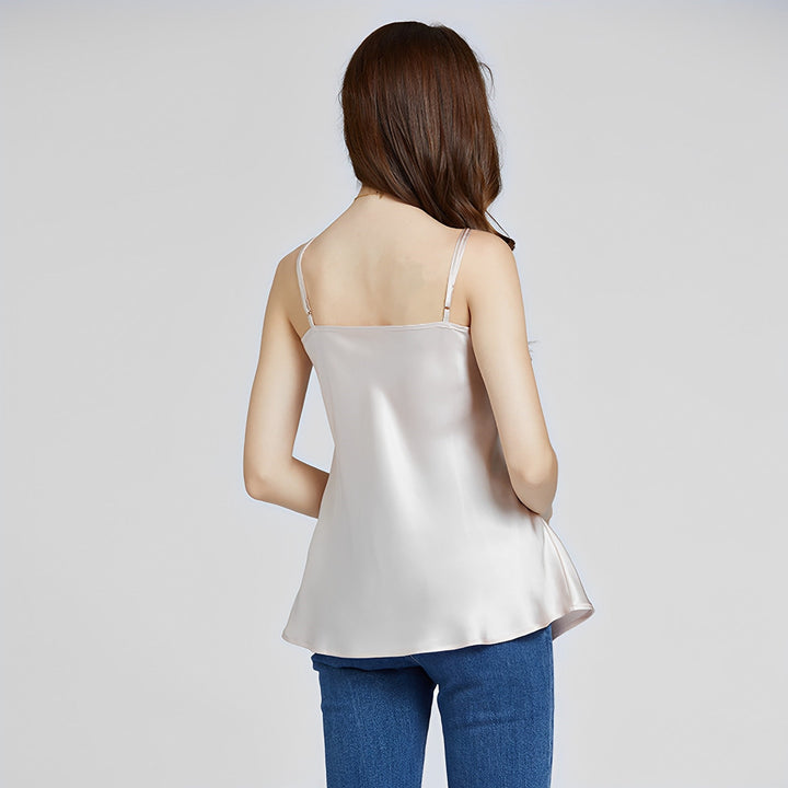 A woman with long brown hair stands with her back to the camera, wearing a light-colored Classic Round Neck Silk Camisole from SusanSilk and blue jeans.